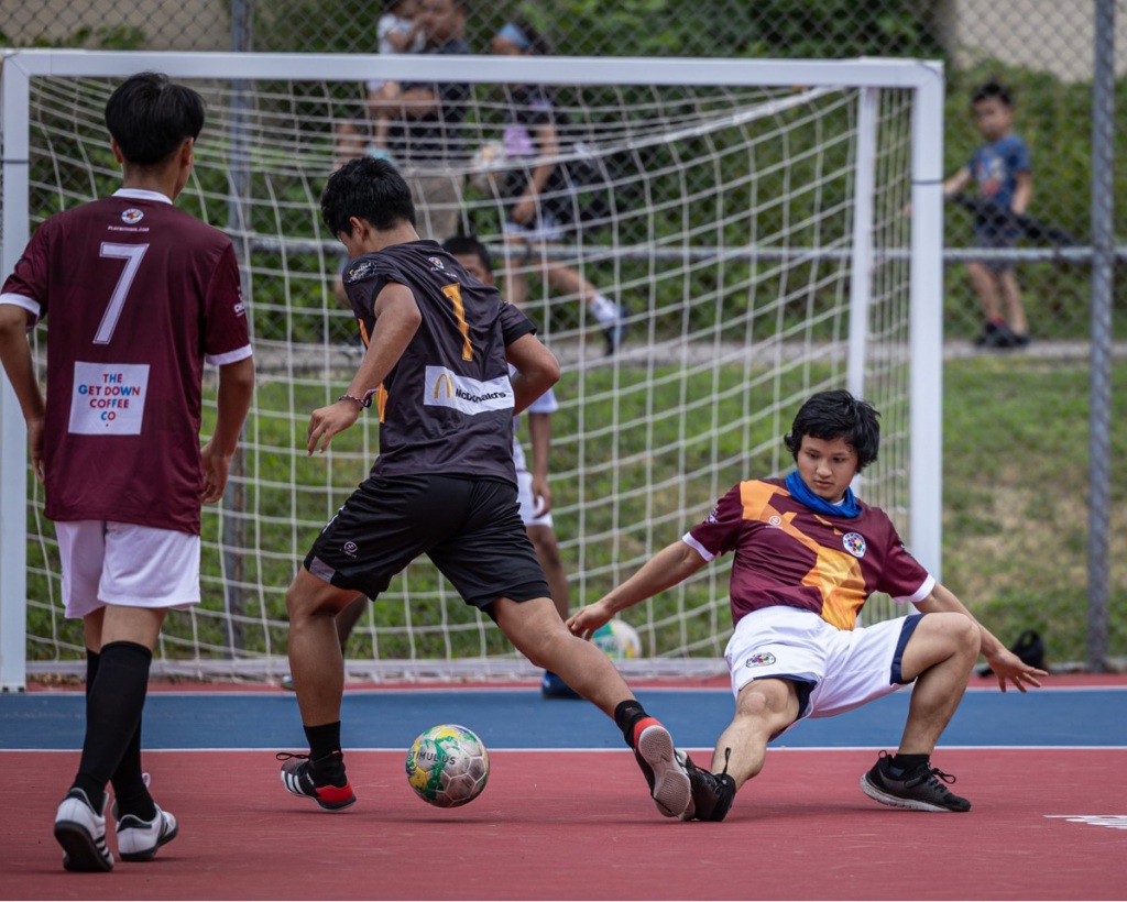 a boy dribbles past a defender who has his leg stretched out across the ground