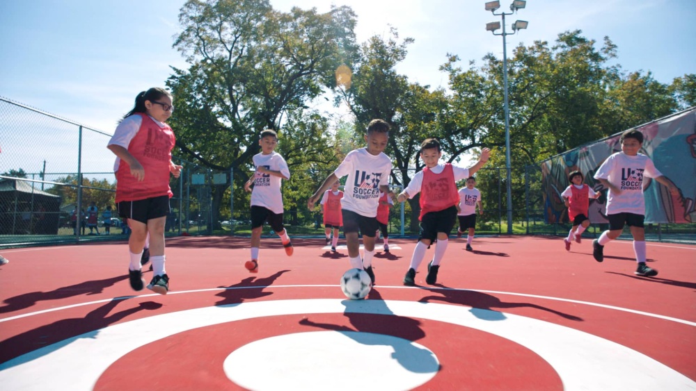 Boys and girls playing soccer on a red and white soccer mini-pitch