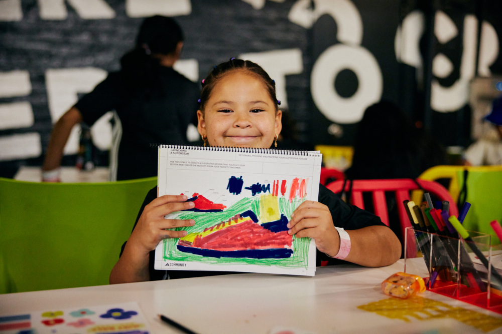 A girl holds up her shoe design and smiles