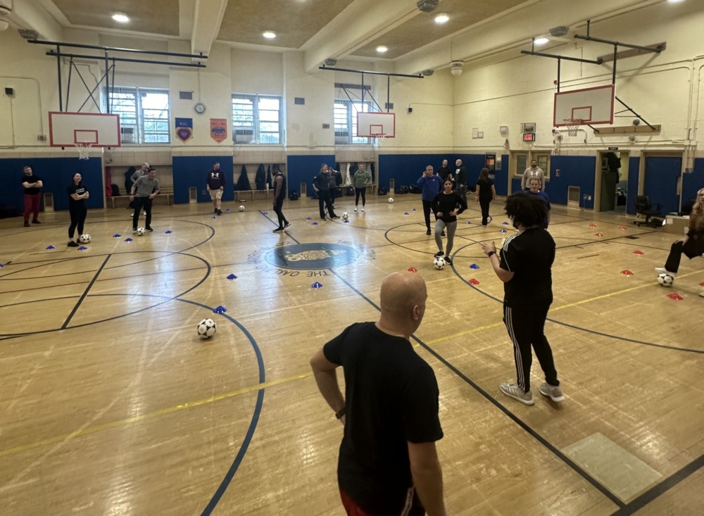 A group of teachers participates in Soccer for Success School training in a gym