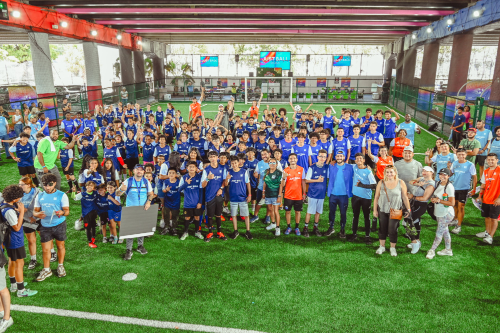 hundreds of youth participants in different color jerseys smile at the camera from the pitch