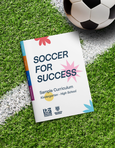 Soccer for success curriculum sitting on a pitch, next to a soccer ball