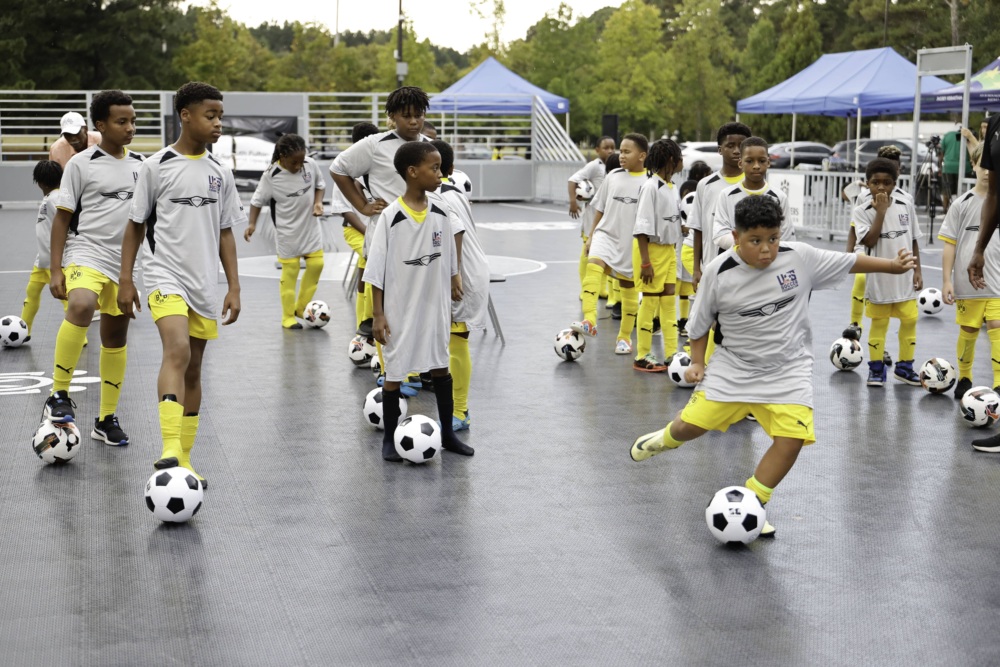 Kids in yellow shorts and gray t-shirts kick balls on mini-pitch