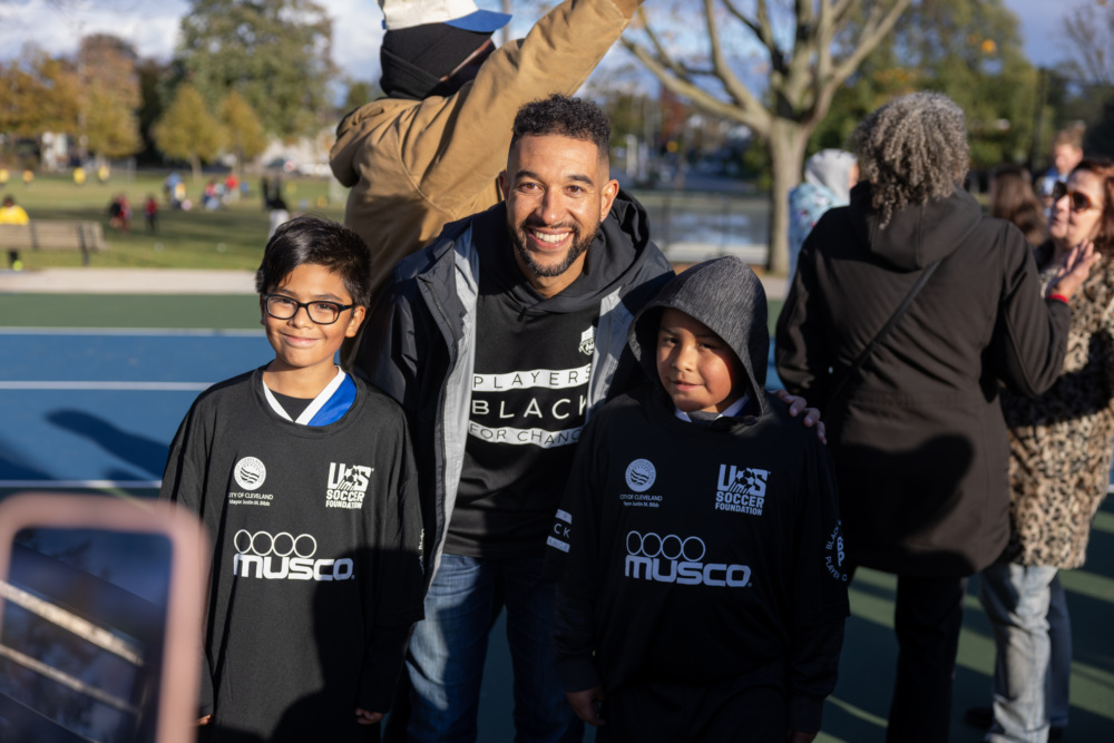 Justin Morrow posing with two smiling kids at a mini-pitch opening in Cleveland