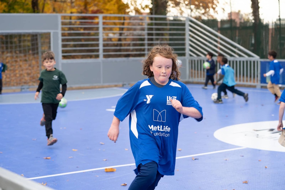 Girl in MetLife/U.S. Soccer Foundation jersey runs across a mini-pitch