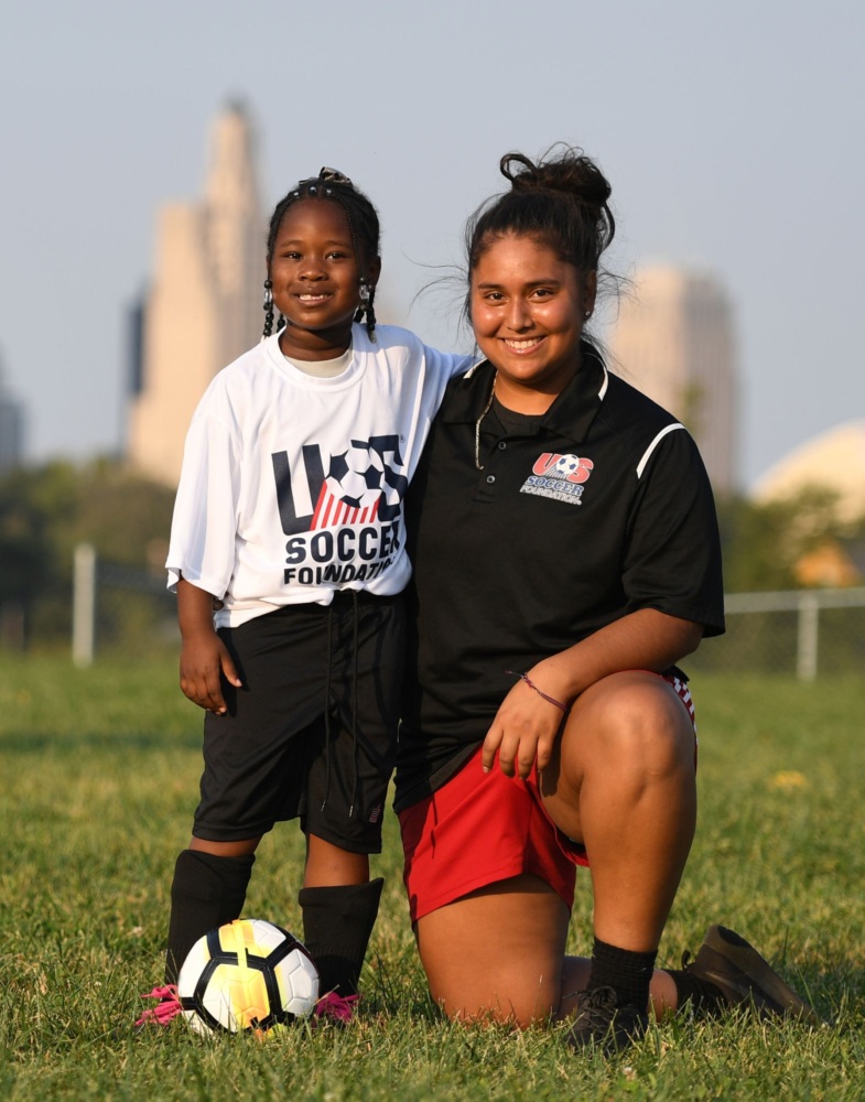 Girl in U.S. Soccer Foundation jersey poses with her coach