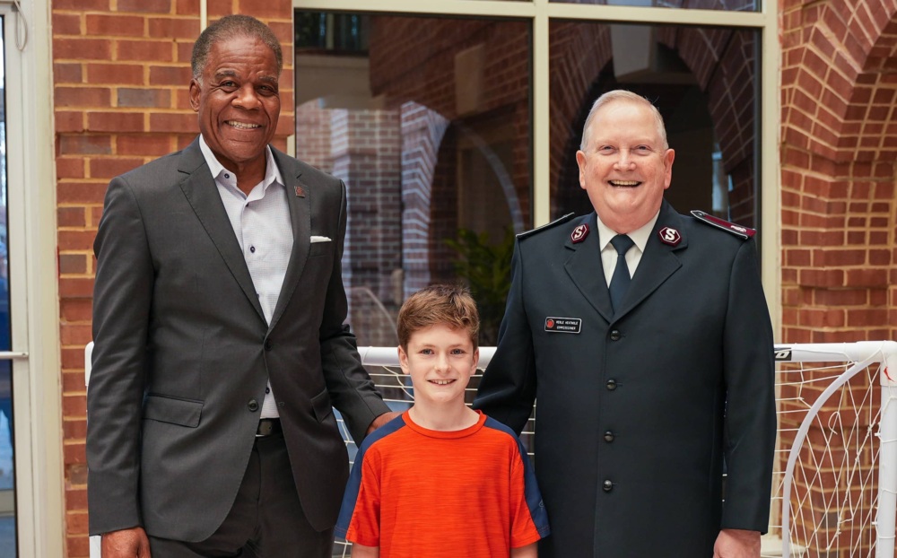 The U.S. Soccer Foundation CEO & President poses with The Salvation Army President & a child dressed in goalie gear