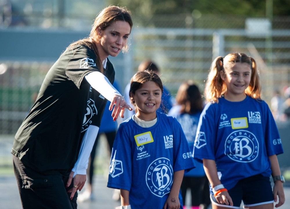 NWSL player coaches kids at mini-pitch opening.