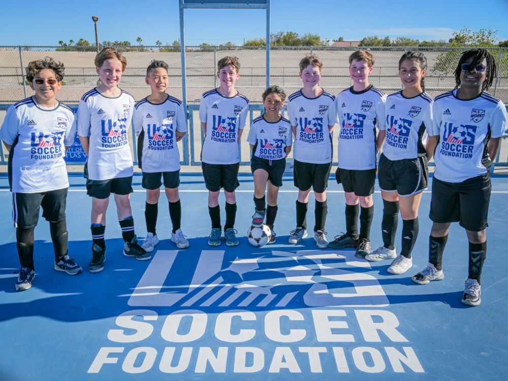 Group of young players stand around U.S. Soccer Foundation logo on a mini-pitch