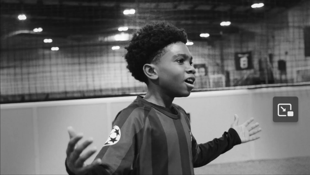 Black and white image of a boy in goalie jersey with arms raised at his sides.