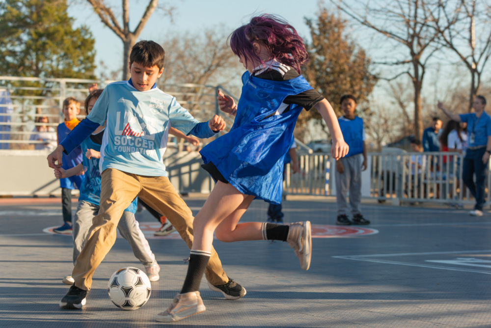 Two kids meet on the pitch, both kicking for the same ball
