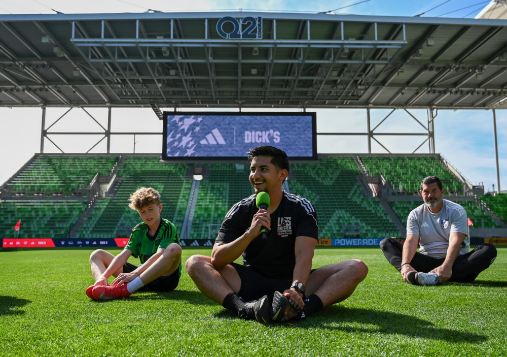 Coach-Mentor Adrian stretches with kids on the field at SXSW community event