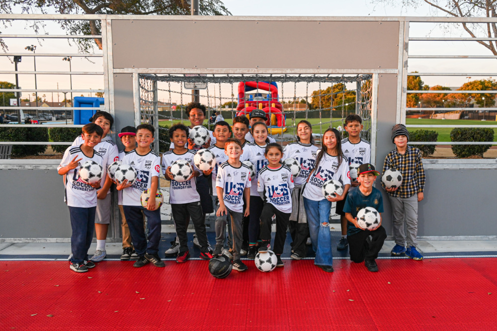kids and adults on a mini-pitch holding soccer balls